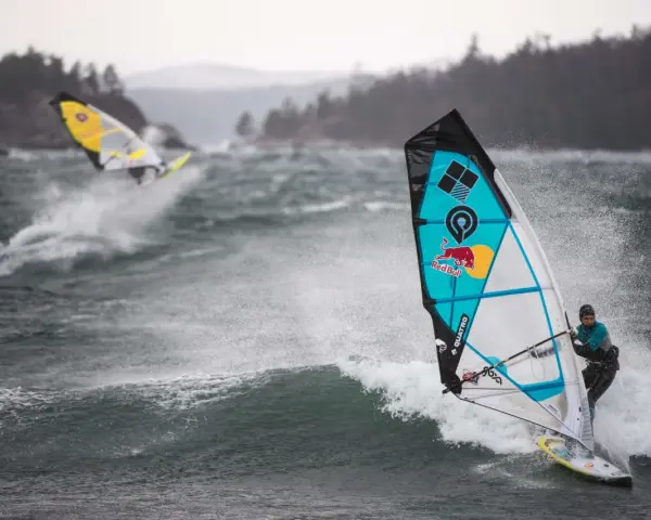Windsurferzy na falach, jeden z nich na pierwszym planie, w akcji.