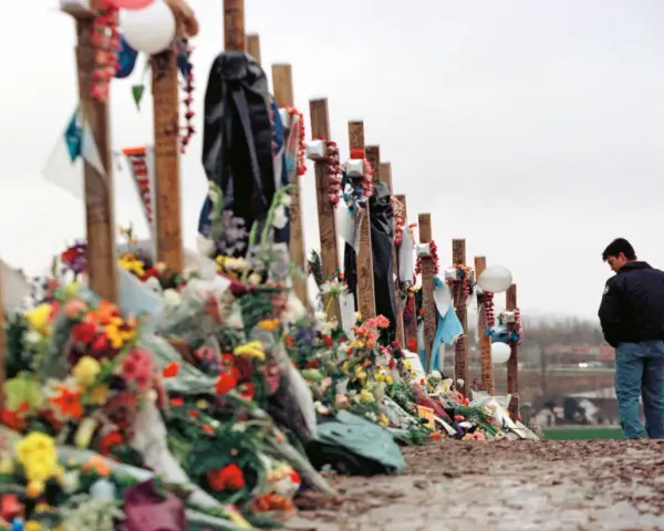 Pamięć o ofiarach masakry w Columbine High School. Krzyże ozdobione kwiatami i pamiątkami, obok stoi pogrążony w zadumie mężczyzna.