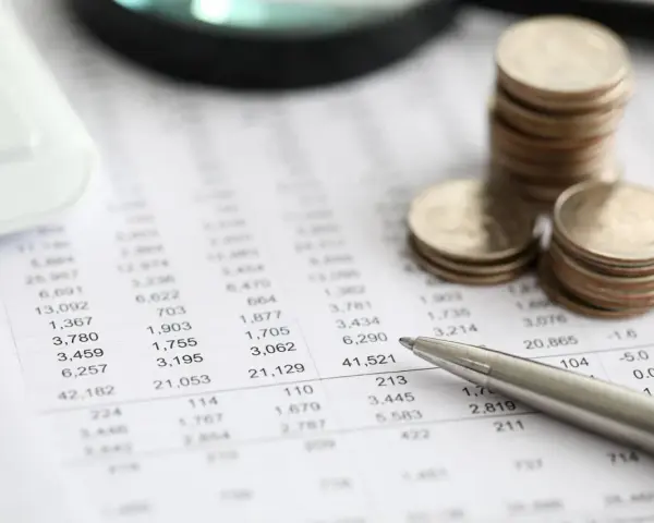Monedas apiladas sobre un informe financiero, con una calculadora y un bolígrafo. El informe muestra números, quizás el modelo 420.