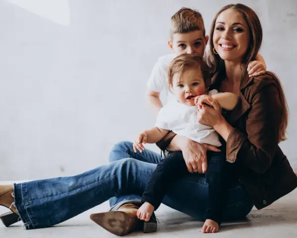 Szczęśliwa mama z dwójką dzieci, maluszkiem na rękach i starszym synkiem za plecami. Idealny urlop na dziecko.