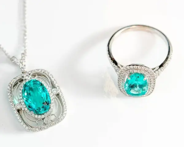Conjunto de collar y anillo con una deslumbrante piedra de geminis turquesa rodeada de diamantes, sobre fondo blanco.