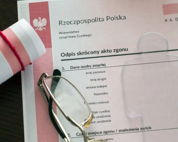 Zrolnowany dokument z orłem, okulary i formularz "Odpis skrócony aktu zgonu".
