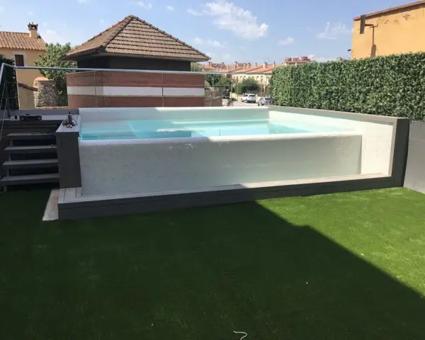 Moderna piscina con mosaico blanco, rodeada de césped artificial y setos. Ideal para decoración de terrazas con piscina.
