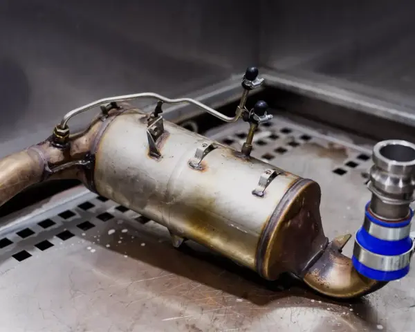 Metalowy element układu wydechowego, prawdopodobnie zapchany dpf, leży na metalowej powierzchni.