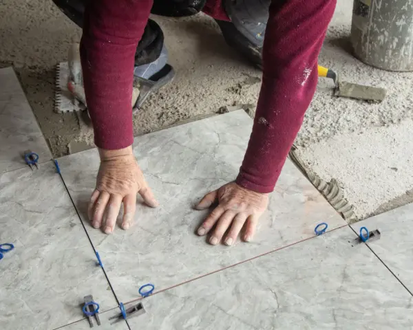 Mani esperte posano mattonelle con precisione, usando livellatori per un risultato perfetto.