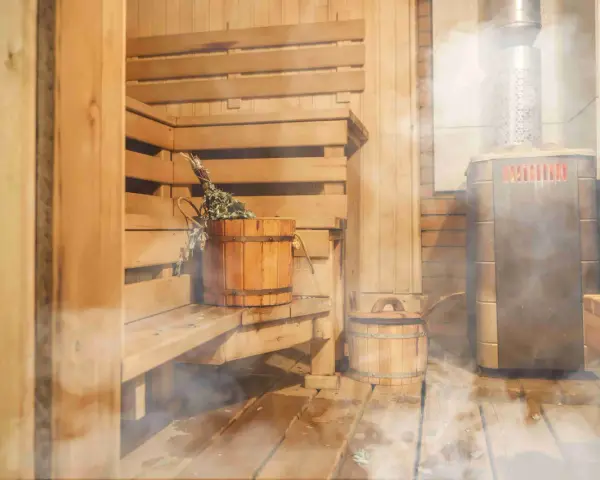 Drewniana sauna z piecem, ławami i wiaderkiem z miotełką. Idealne miejsce, by dowiedzieć się, jak zbudować saunę i odpocząć.