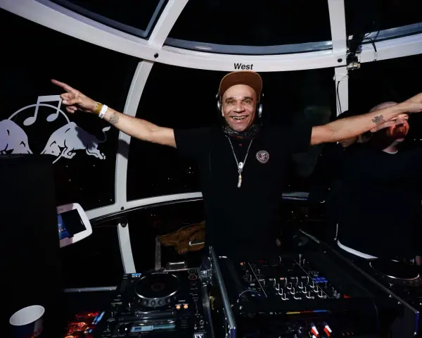 Un dj rap souriant, casqué, bras écartés, anime la soirée dans une cabine panoramique.