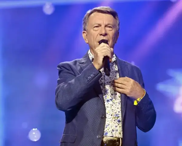 Wojciech Gąsowski w niebieskiej marynarce w kropki i kwiecistej koszuli śpiewa na scenie.