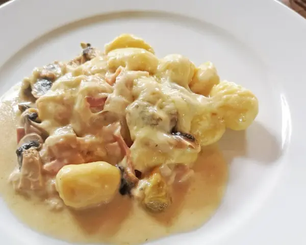 Gnocchi al forno mit cremiger Käsesauce, Pilzen und Schinken auf einem weißen Teller.