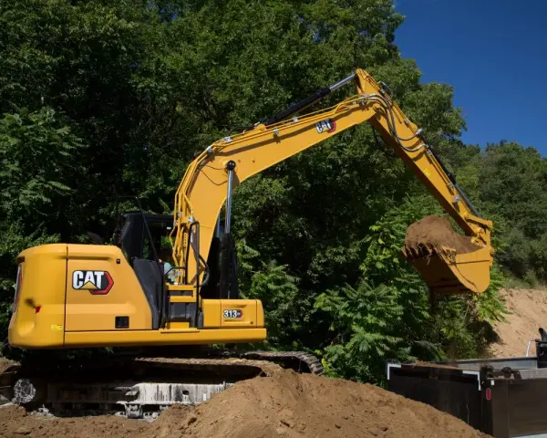 Żółta koparka Cat 313 z łyżką pełną ziemi, gotowa do pracy. Dane techniczne tej maszyny budowlanej są imponujące.