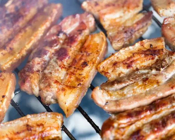Kawałki soczystego boczku surowego pieką się na grillu, otoczone dymem.