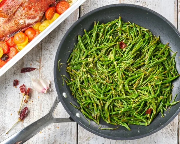Asparagi di mare saltati in padella con aglio e peperoncino, accanto a un pesce al forno con pomodorini.