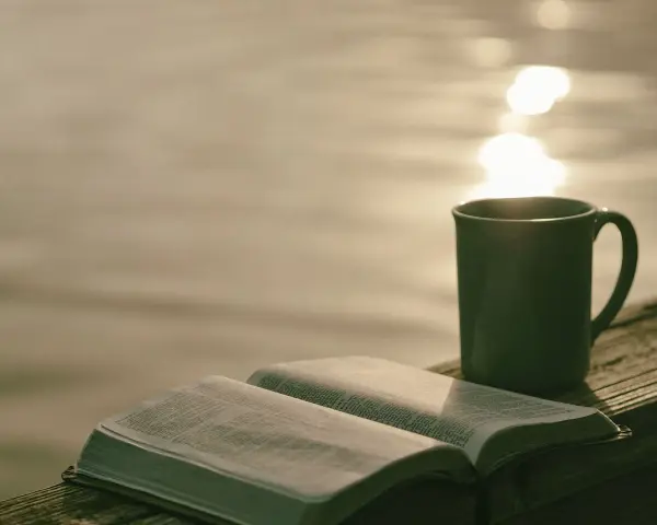 Offenes Buch mit Bibelversen, Tasse Kaffee am Seeufer. "Ich liebe den Herrn, denn er hört meine Stimme" (Psalm 116:11).