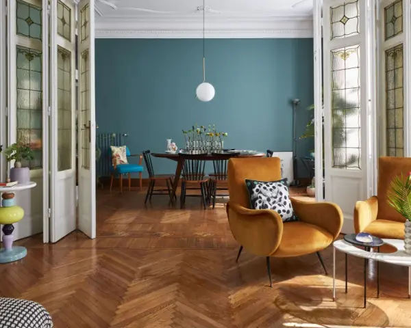 Salotto con un mix di arredamento moderno e antico: poltrone ocra, tavolino colorato, porte a vetri d'epoca e un tavolo da pranzo in stile classico.