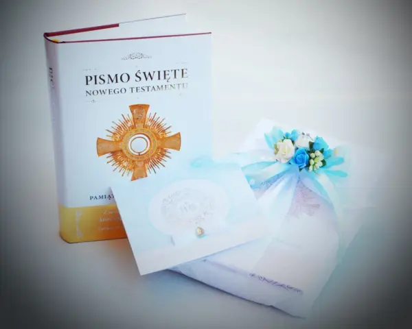 Dedykacja na komunię: Pismo Święte, ozdobna kartka i prezent z błękitną wstążką i kwiatami.