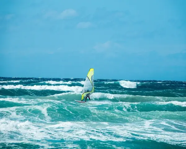 Windsurfer na wzburzonym, turkusowym morzu pod błękitnym niebem.
