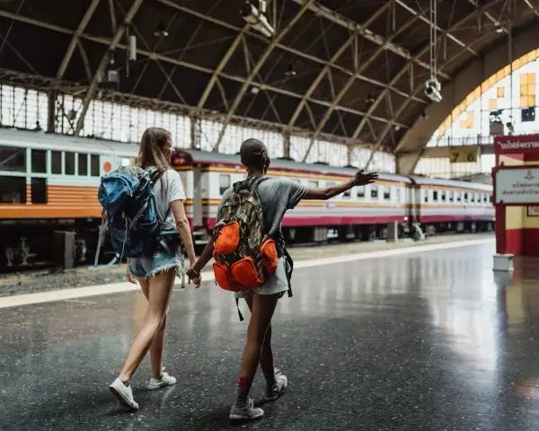 Dwie podróżniczki z plecakami idą wzdłuż peronu, gdzie stoi długi pociąg. Może to być ich pierwszy pociąg Eurostar.
