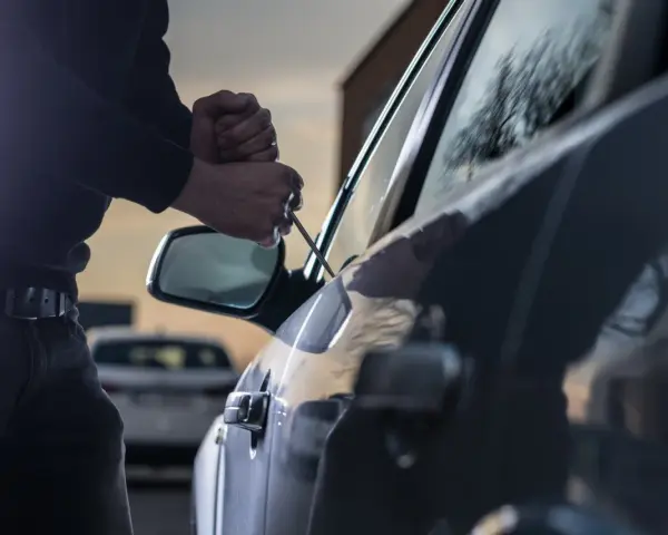 Tentativo di furto d'auto: un uomo usa un cacciavite per forzare la portiera, un'azione che rientra nella verifica veicoli rubati.