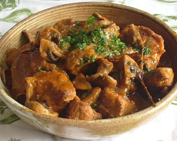 Un délicieux sauté de veau aux champignons, garni de persil frais, servi dans un bol en terre cuite.