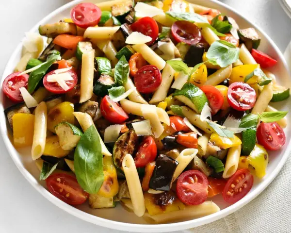 Bunter Nudelsalat ohne Mayo mit Penne, gegrilltem Gemüse wie Zucchini, Aubergine, Paprika, Kirschtomaten und frischem Basilikum, garniert mit Parmesan.