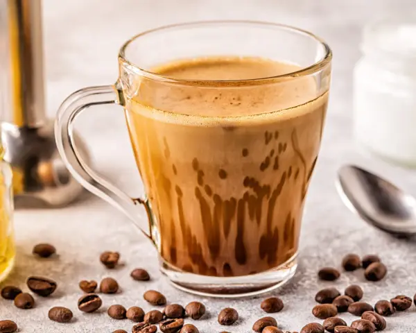 Kawa bullet coffee w szklance, obok ziarna kawy, słoiczek z miodem i łyżeczka.