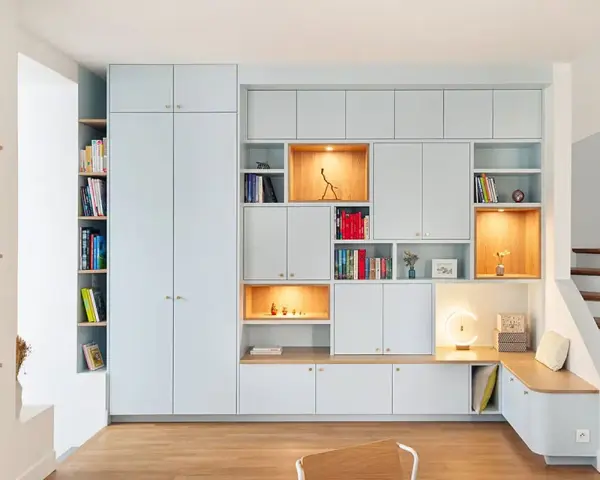 Aménagement d'un **pièce à vivre** moderne avec bibliothèques modulables, rangements intégrés et un banc cosy près de l'escalier.