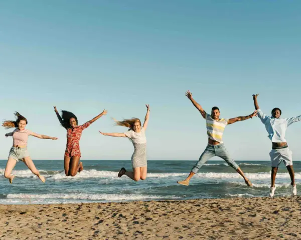 Fünf junge Leute springen ausgelassen am Strand. Sie freuen sich über ihr Sprachreise Stipendium und die Freiheit.