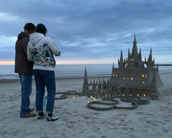 Para podziwia imponujące zamki z piasku na plaży, w okolicach Kołobrzegu. Wieczorne światła dodają magii.
