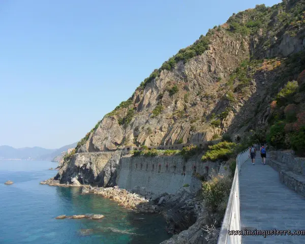 Wanderer auf dem Sentiero Azzurro entlang der felsigen Küste Liguriens. Das Meer glitzert türkisblau neben dem steilen Hang.