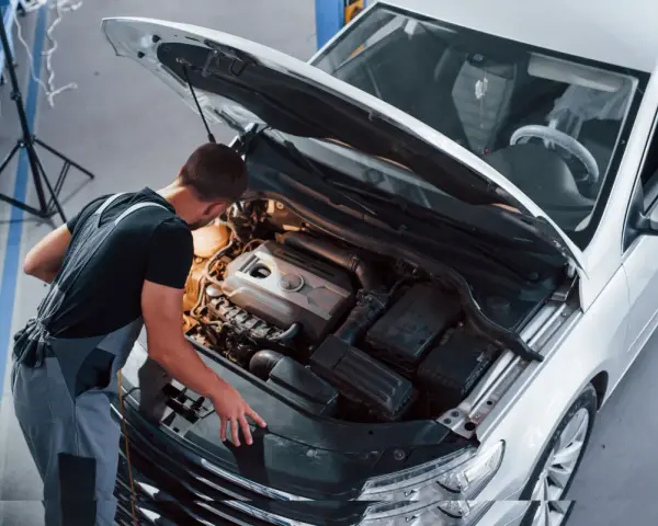 Młody mechanik w kombinezonie pracuje przy silniku białego samochodu. To jego pasja, każdy konstruktor marzy o takiej precyzji.