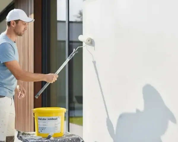 Mann streicht Fassade mit weißer Farbe. Für ein gleichmäßiges Ergebnis ist eine Grundierung notwendig.
