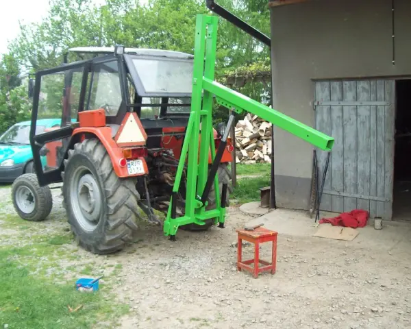 Czerwony traktor z zamontowanym zielonym ładowaczem TUZ przed budynkiem gospodarczym.