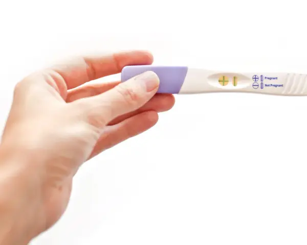 Dłoń trzyma test ciążowy z wynikiem pozytywnym. W okienku widoczny jest symbol plusa, oznaczający ciążę.