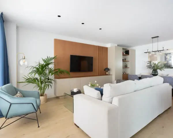 Un elegante salón moderno blanco con sofá, sillón azul, planta y mesa de comedor.