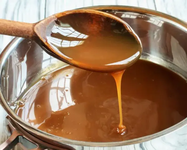 Caramelo líquido cayendo de una cuchara de madera a una olla, perfecto para tu flan al estilo Eva Arguiñano.
