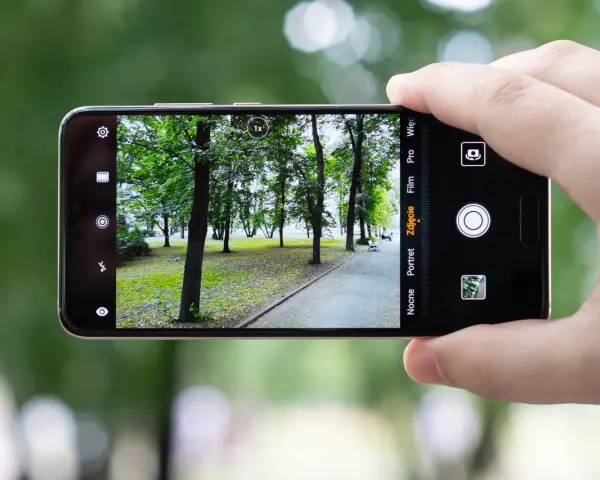 Dłoń trzyma smartfon Huawei P20, aparat kadruje parkowy krajobraz z alejką i drzewami.