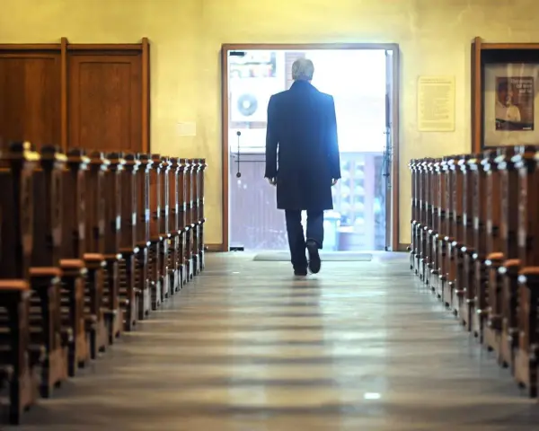 Mann verlässt Kirche in NRW. Er geht durch den Gang zwischen den Kirchenbänken zum Ausgang.