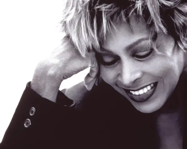 Tina Turner lächelt mit geschlossenen Augen, die Hand am Kopf. Ein ikonisches Bild der Musiklegende.