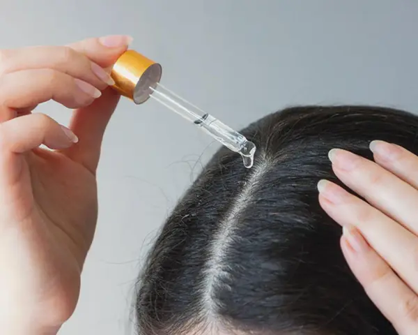 Eine Hand trägt mit Pipette ein Serum auf die Kopfhaut auf, um trockene Schuppen loswerden.