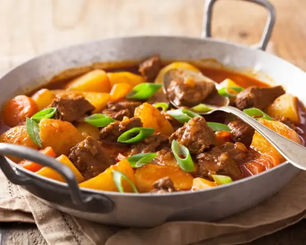 Estofado de ternera tierno con patatas y zanahorias en una sartén, adornado con cebolleta.