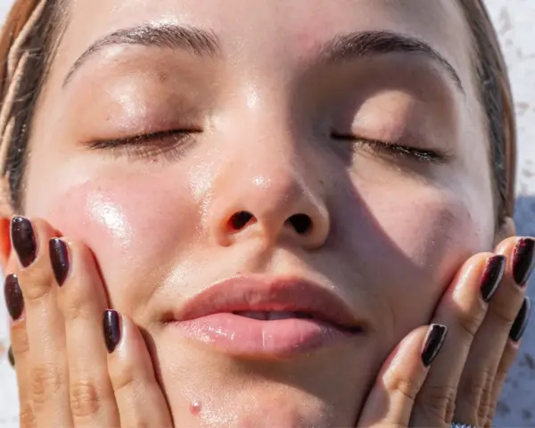 A woman's face, with eyes closed and skin glowing, touches her cheek. It makes you wonder, can your skin type change with the seasons?