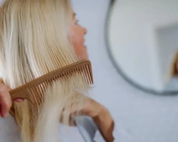 Kobieta czesze blond włosy, szukając rozwiązań co na wypadanie włosów po ciąży.