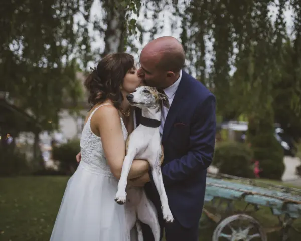 Un couple s'embrasse tendrement, tenant leur chien, dans cette photo de mariage.