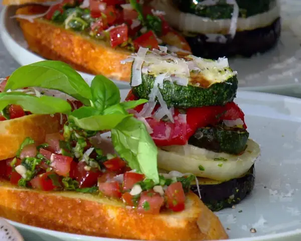 Vegane Grillrezepte: Bruschetta mit Tomaten und gegrilltem Gemüse-Turm, garniert mit Basilikum und Parmesan.