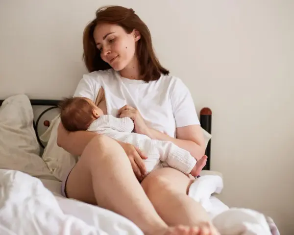 Matka karmi piersią dziecko na łóżku. To piękny obrazek z okresu 12-miesięczny okres ochronny po urlopie macierzyńskim.