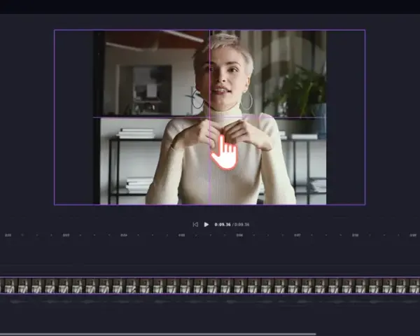 Kobieta w białym golfie, siedząca i mówiąca, z dłonią wskazującą na ekran edytora wideo.