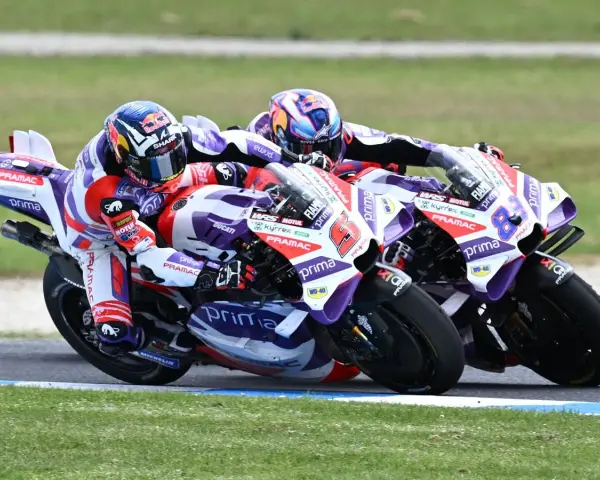 Dos pilotos de MotoGP compiten en una carrera emocionante. El piloto número 6, con casco rojo y blanco, lidera, seguido de cerca por el número 88.
