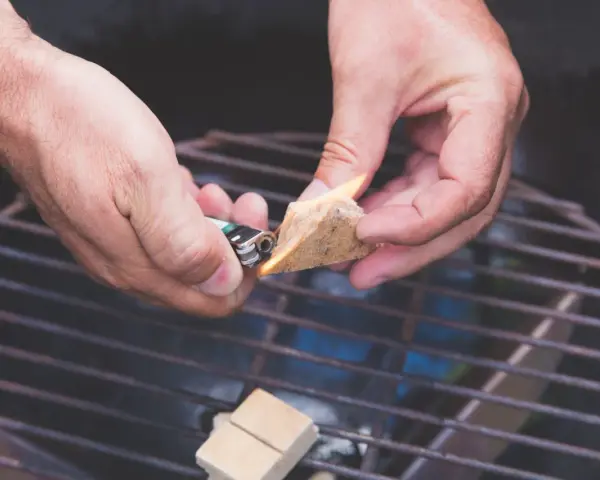 Hände zünden Grillanzünder an, um den Grill anzufeuern.