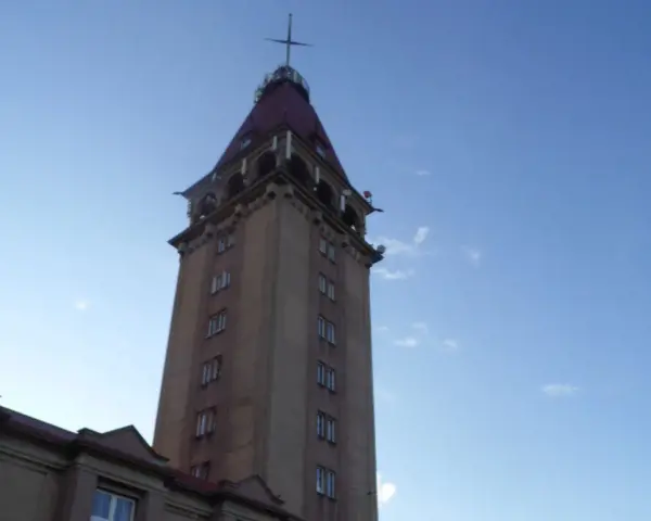 Wysoka wieża z czerwonym dachem, przypominająca dom rybaka, na tle błękitnego nieba.
