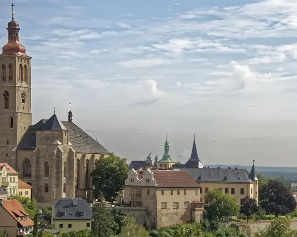 Majestatyczna katedra i zabytkowe budynki w Kutnej Horze pod błękitnym, chmurnym niebem.